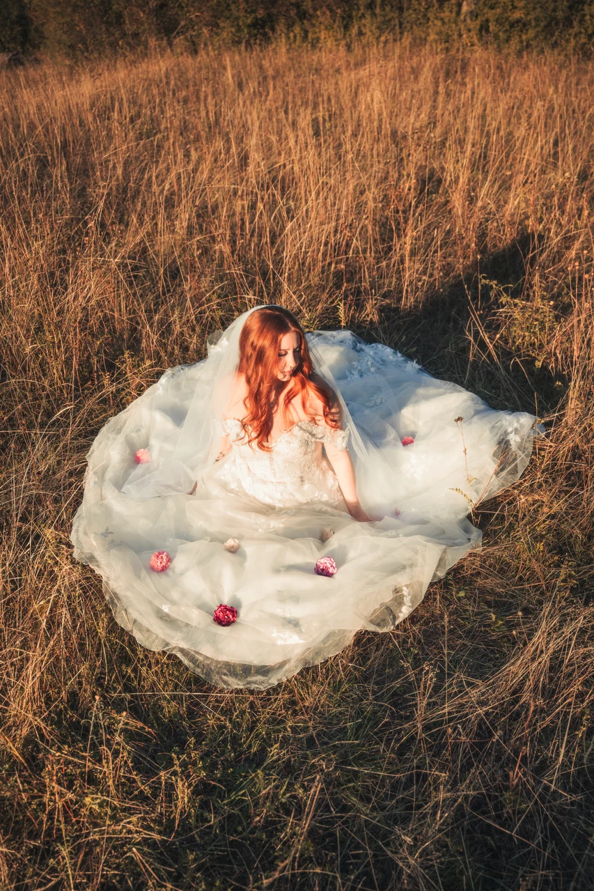 Braut mit ausgebreitetem Kleid und Blüten auf einer Wiese im goldenen Abendlicht