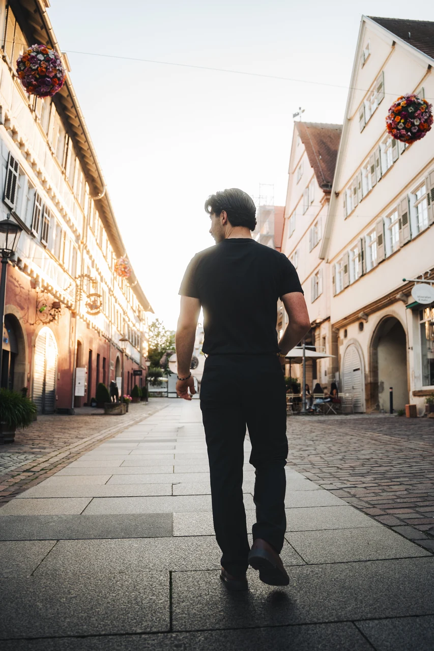 Mann in schwarzem Outfit beim Gehen durch eine Altstadt im warmen Abendlicht